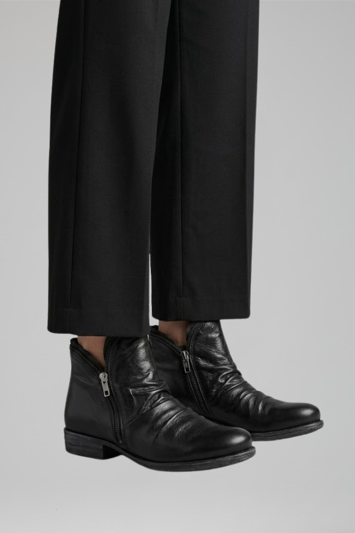 Black leather boots worn with black pants on a gray background