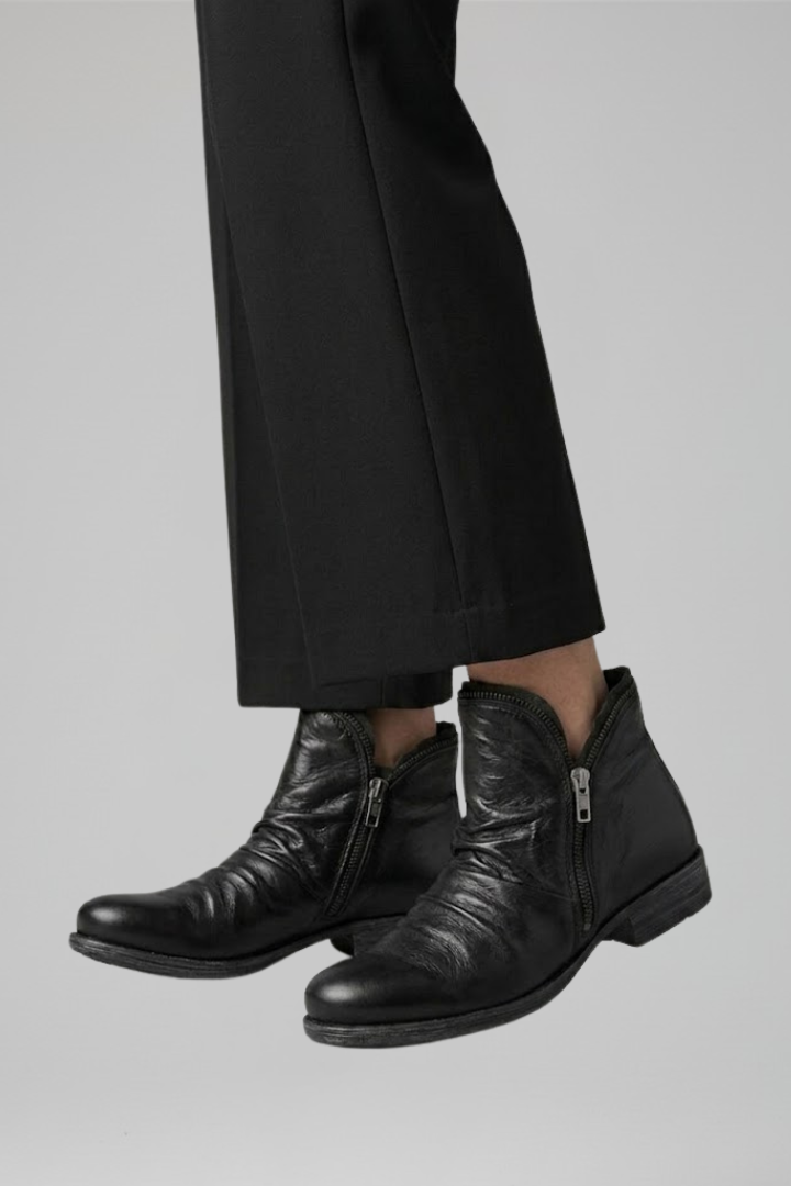 Black leather boots worn with black pants on a gray background