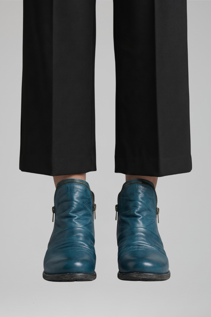 Teal leather boots worn with black pants on a light gray background