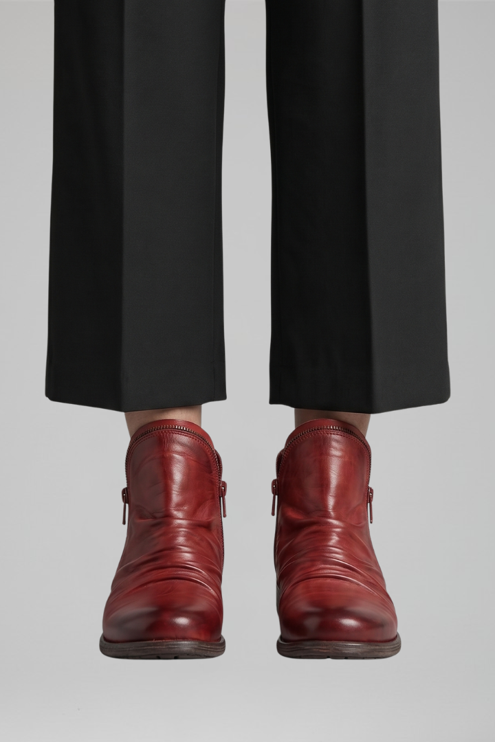 Red leather boots worn with black pants on a light gray background