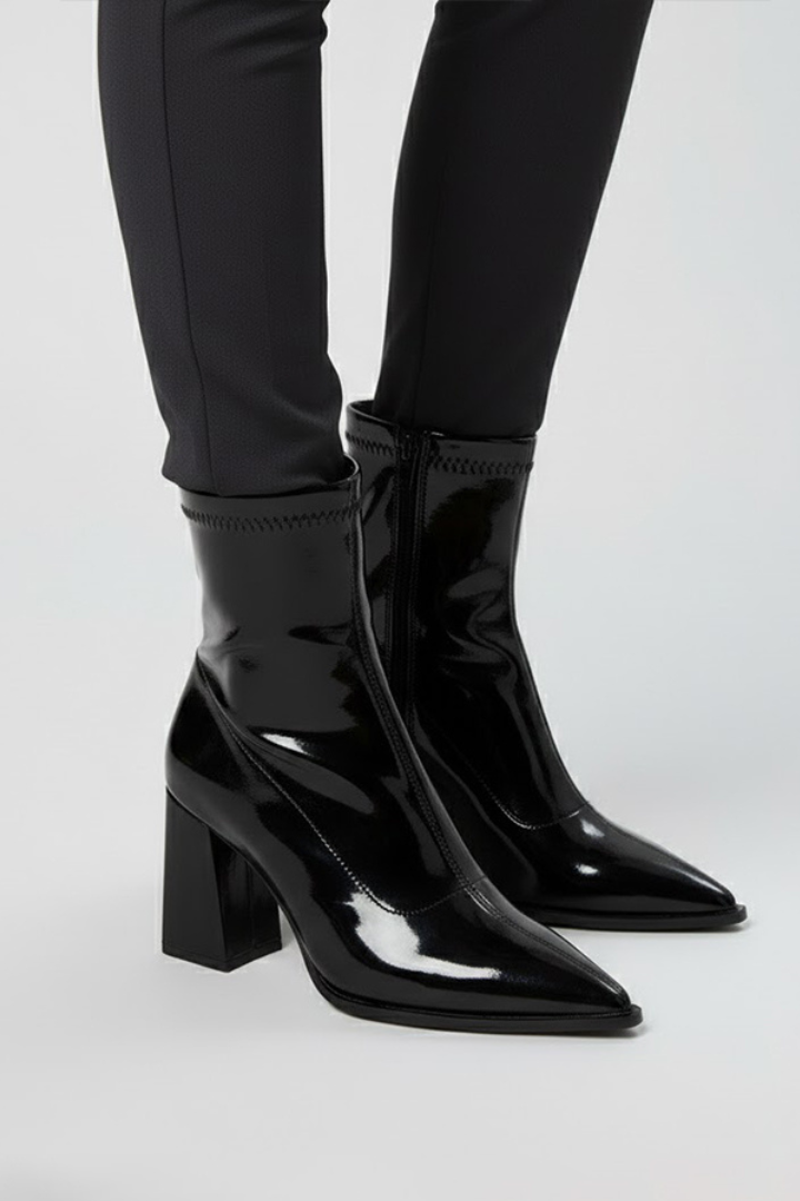 Black patent leather boots worn with black pants on a white background