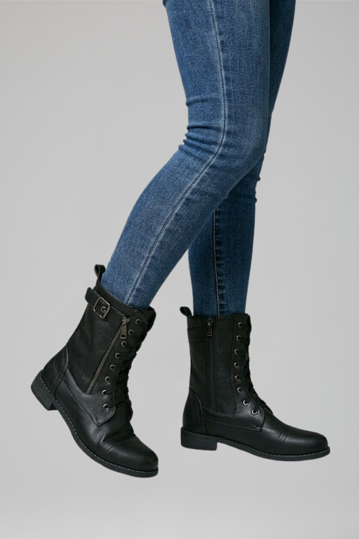 Black leather boots worn with blue jeans on a gray background