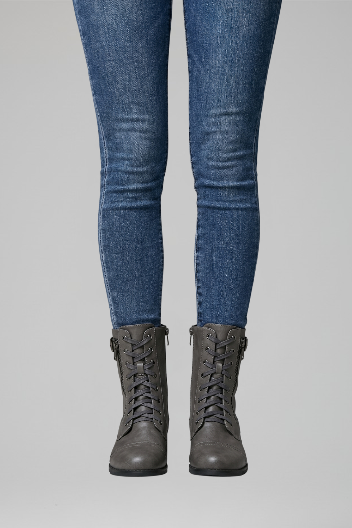 Person wearing blue jeans and gray combat boots on a light gray background