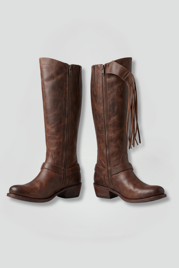 Pair of brown leather knee-high boots with fringes on a light gray background